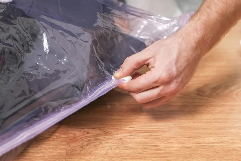 A man places winter clothing in a vacuum-sealed bag for storage.