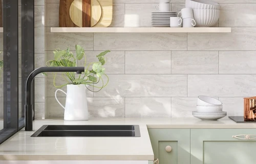 A cozy, clean kitchen with a black sink and tan countertops, with overhead shelving holding assorted dishes.