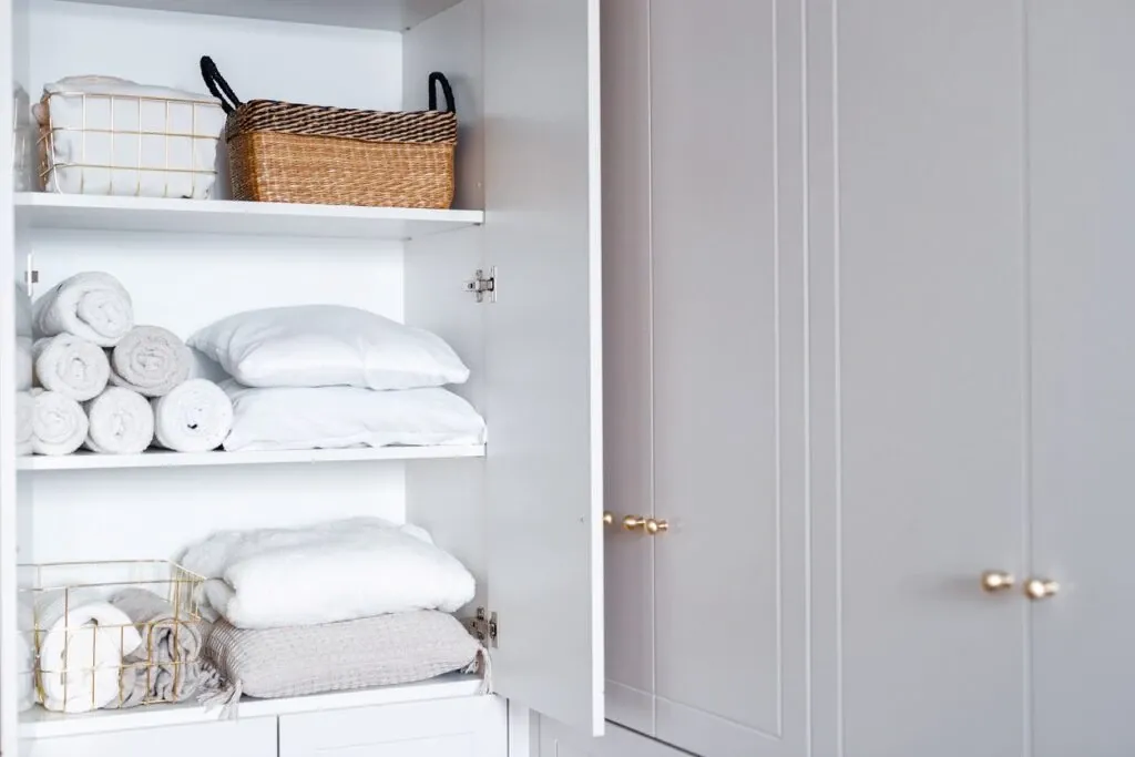 Several white towels, sheets, and pillows neatly folded and organized in an apartment cabinet. 
