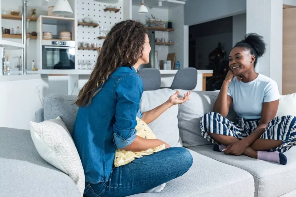 Two young women sitting on a couch engaging in conversation.