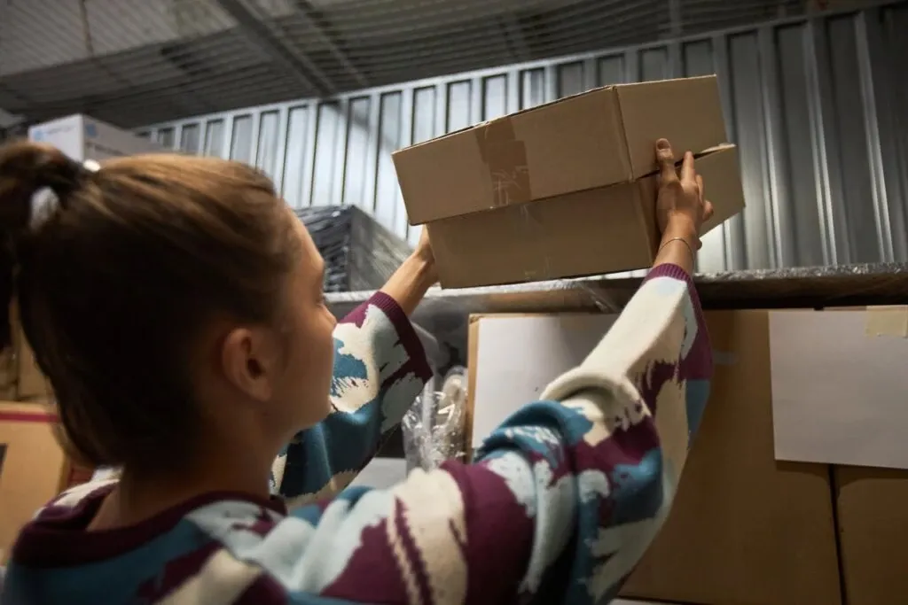 A woman with a ponytail places a box of stored items on a shelf in her self storage unit.