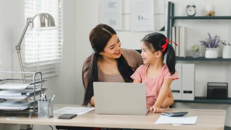Smiling mother and daughter bonding at laptop in a home office.