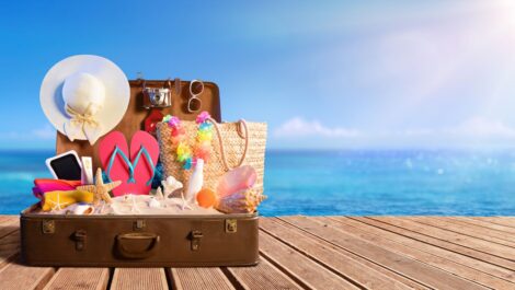 Summer items in a suitcase set on a dock near the ocean shore.