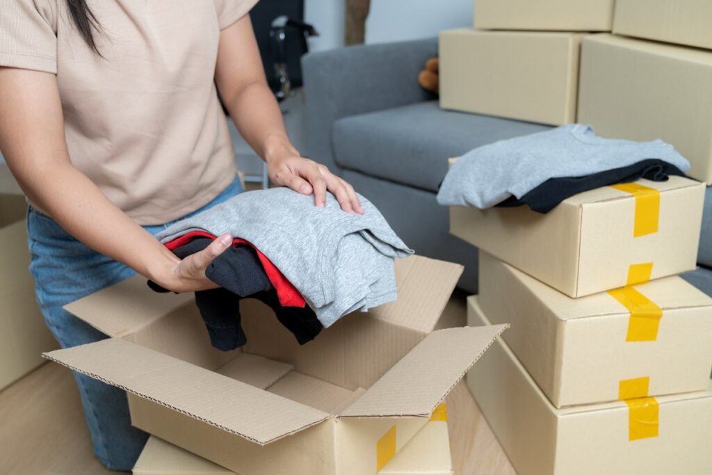 A woman folding and packing her summer clothing into cardboard boxes.