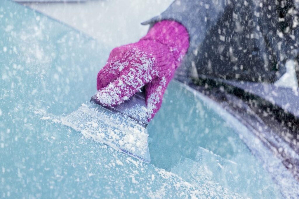A person using an ice scraper to clean off their windshield.