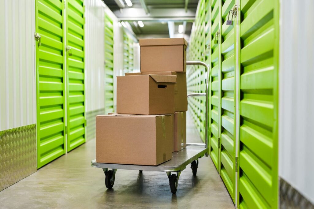 Five cardboard boxes on a cart in a hallway of neon green self storage units. 