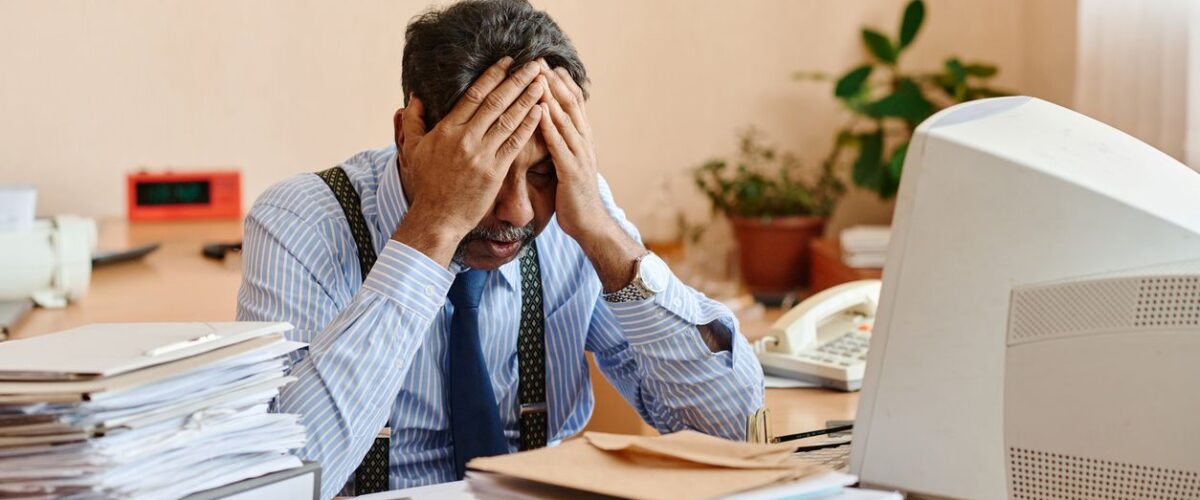 A stressed middle-aged man at a disorganized desk.