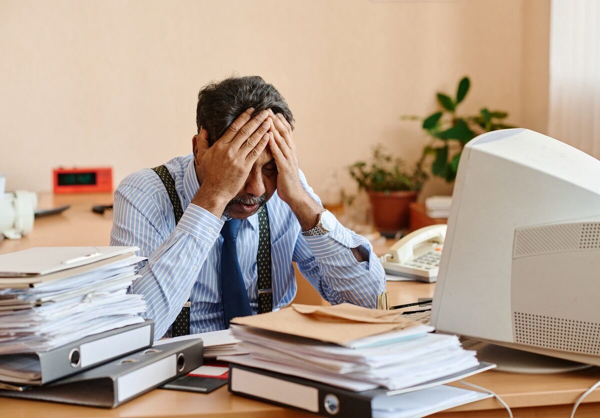 A stressed middle-aged man at a disorganized desk.