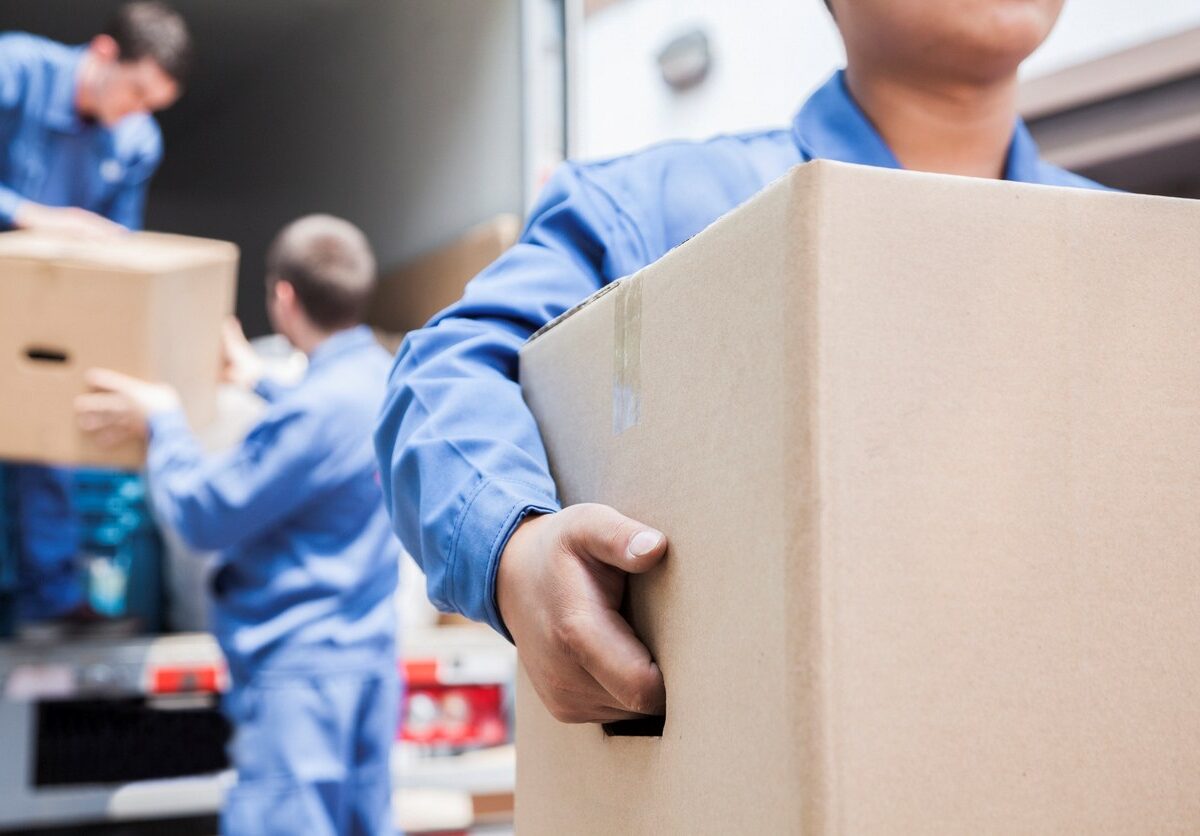 A group of workers in blue uniforms loads cardboard boxes into a moving truck.